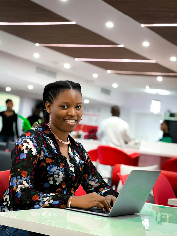 A young Nigerian woman smiling at her laptop in a bright study space